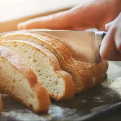 Dłoń kroi świeży chleb na kromki. Dowiedz się, jak odświeżyć chleb, by znów był pyszny.