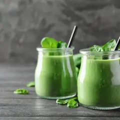 Dwa słoiczki pysznego, zielonego smoothie ze szpinakiem, udekorowane świeżymi liśćmi. Idealne na zdrowy początek dnia.