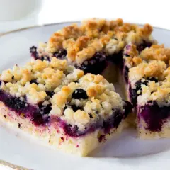 Szybkie ciasto z borówkami i kruszonką na talerzu, obok szklanka mleka. Idealne na deser.