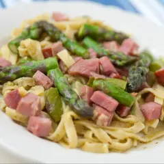 Pyszne tagliatelle ze szparagami i kawałkami szynki, podane na białym talerzu.