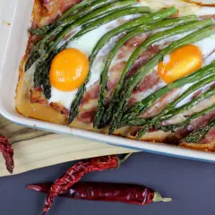 Pyszne śniadanie ze szparagami, jajkami i boczkiem zapieczone w naczyniu. Obok suszone papryczki chili.
