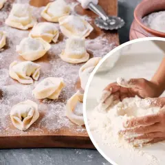 Ręce mieszają mąkę, przygotowując ciasto na pierogi. Na desce leżą gotowe pierożki, posypane mąką.