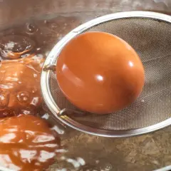 Jajka na miękko czas! Brązowe jajka gotują się w bulgoczącej wodzie, jedno z nich jest wyciągane sitkiem.