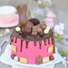 Różowy tort z czekoladowym dripem, ozdobiony zajączkami z czekolady, jajeczkami i ciasteczkami. Idealny na Wielkanoc!