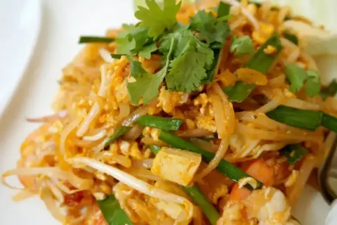 Pyszne makaron po tajsku z krewetkami, tofu, jajkiem i szczypiorkiem, udekorowany świeżą kolendrą.
