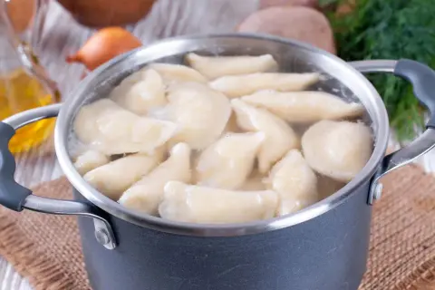Gotowanie pierogów w garnku. Woda wrze, a pierogi unoszą się na powierzchni. W tle widać olej i koperek. Dowiedz się, ile gotować pierogi, by były idealne.