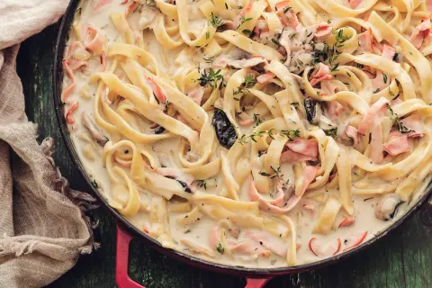 Tagliatelle w kremowym sosie z kawałkami szynki i grzybów, pachnące tymiankiem. Pyszne mac and cheese w nowej odsłonie.