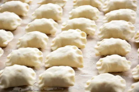 Rządki surowych pierogów z farszem na pierogi ruskie, gotowe do gotowania.