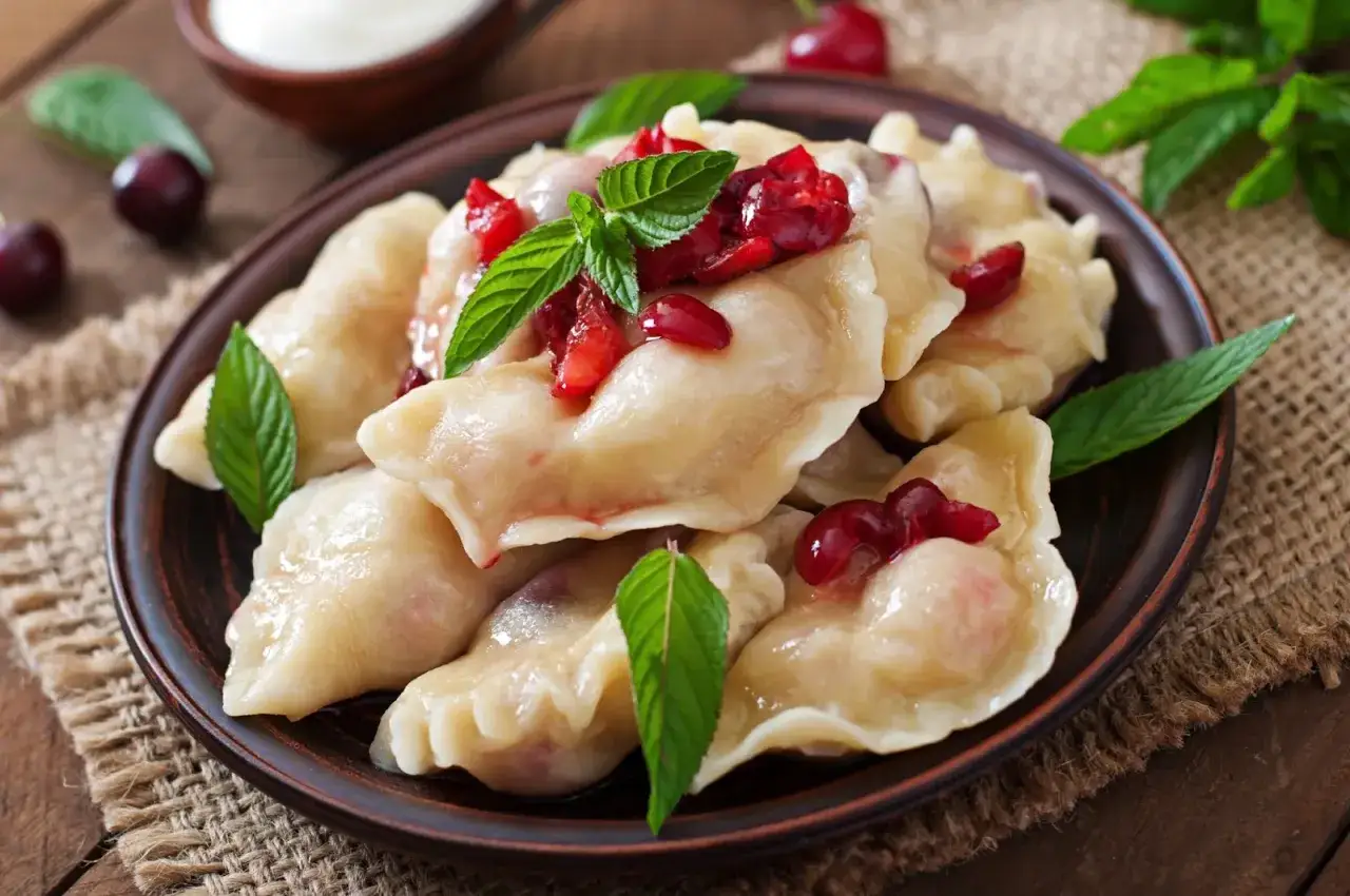 Pyszne pierogi z wiśniami, ozdobione miętą. Idealne na deser! Wiesz, ile gotować pierogi, by były idealne?